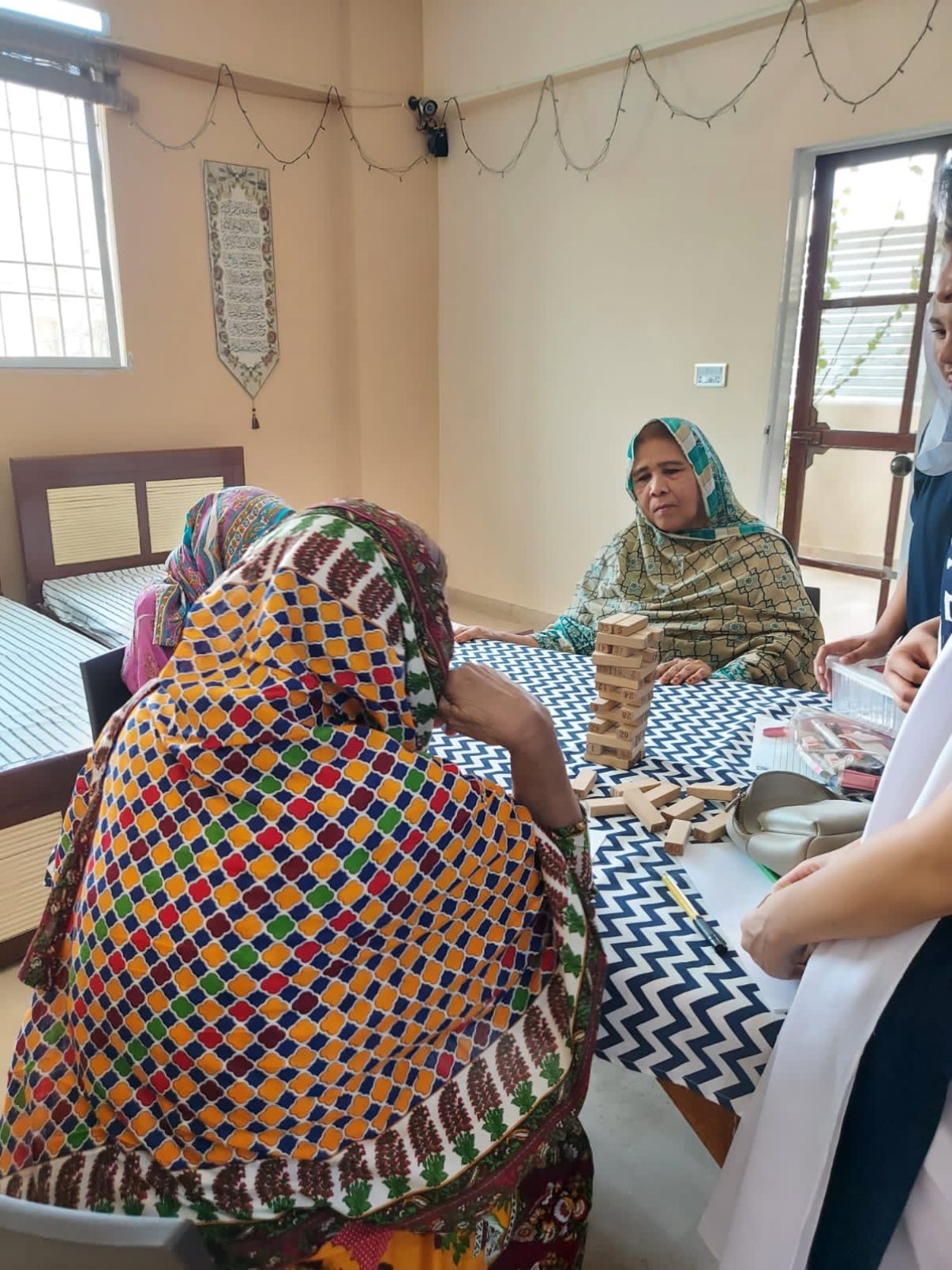 A resident and a visitor playing a wooden block-stacking game at a table with a patterned cloth