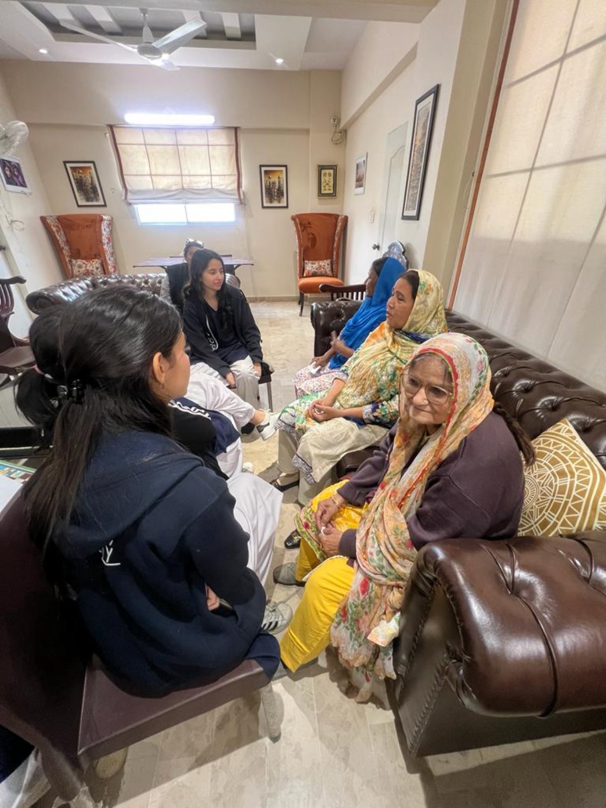 Residents seated on a leather sofa talking with student volunteers in a sitting room